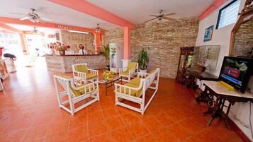 A hotel lobby with white wicker furniture, a reception desk, and a television.