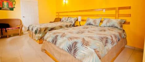 Habitación de hotel con dos camas, una silla, una puerta y una pared con un mural tropical.