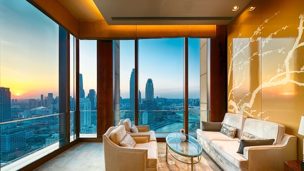 A spacious room with a large window offering a city view, a sofa, a chair, and a glass coffee table. - Shangri-La Tianjin (Tianjin)