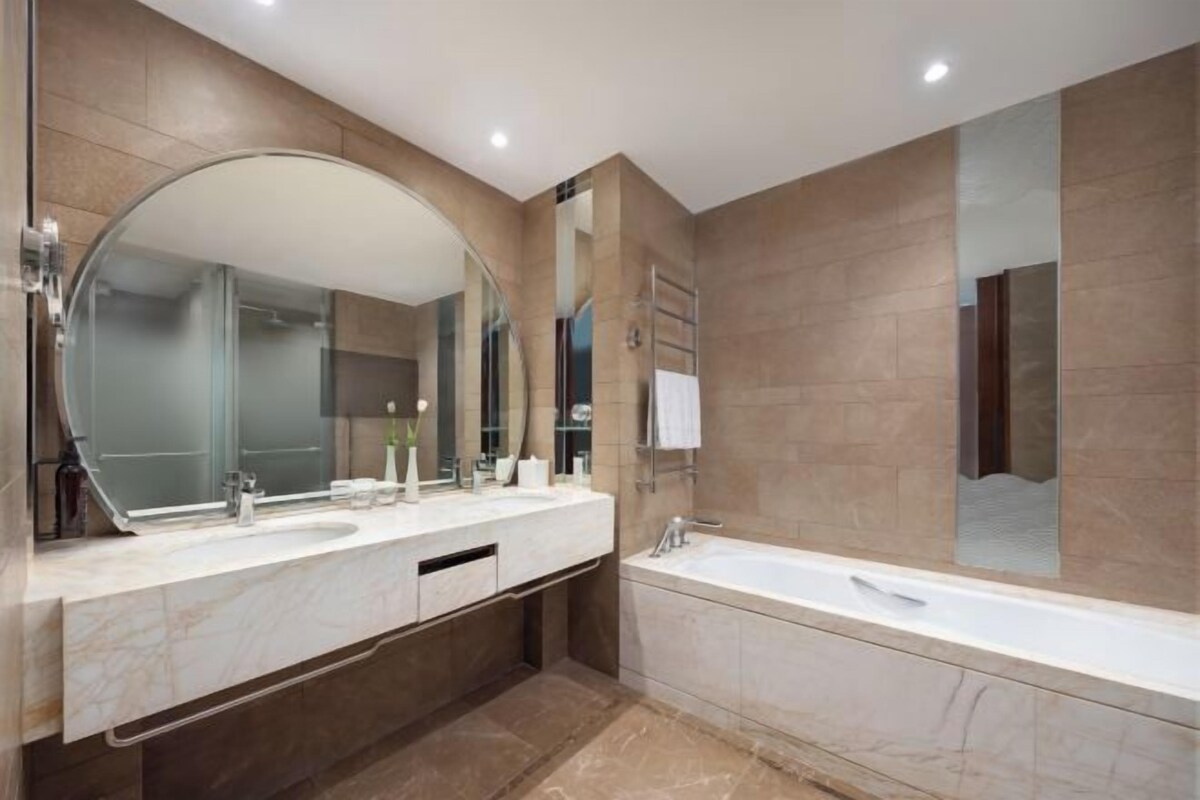 A modern bathroom with a large mirror, two sinks, a bathtub, and a towel rack.