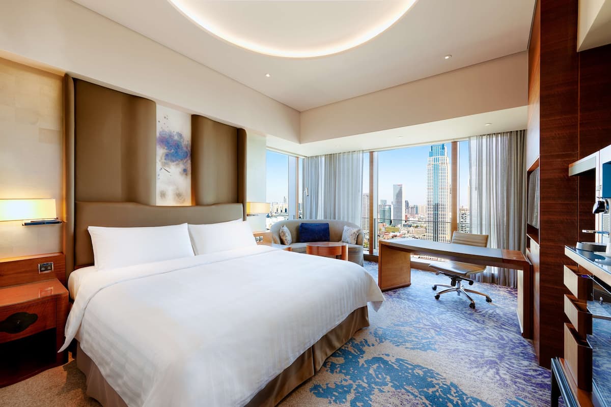 Quarto de hotel com uma cama grande, uma escrivaninha, uma cadeira e vista para a cidade.