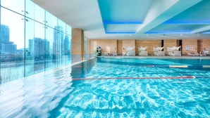 An indoor swimming pool with clear blue water, wooden panel walls, and a city view through large windows. - Shangri-La Tianjin (Tianjin)