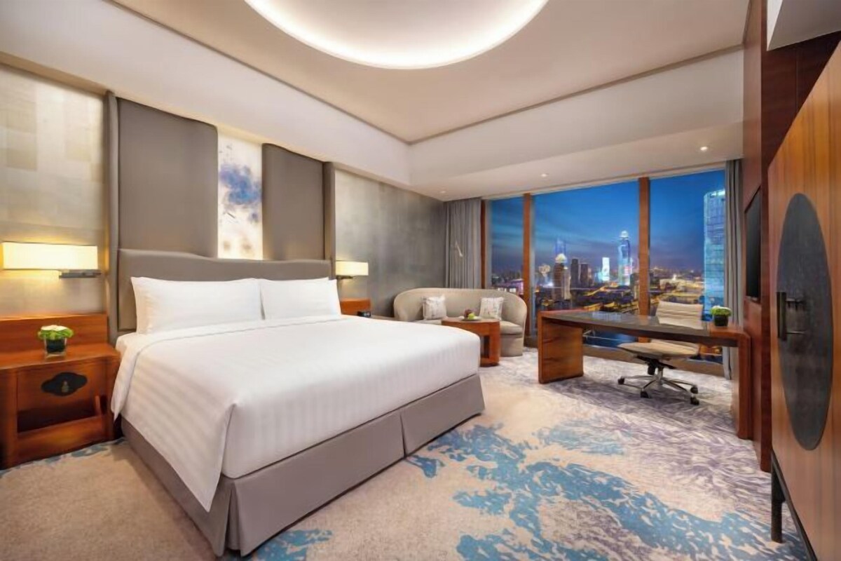 A hotel room with a large bed, a desk, and a view of a cityscape.