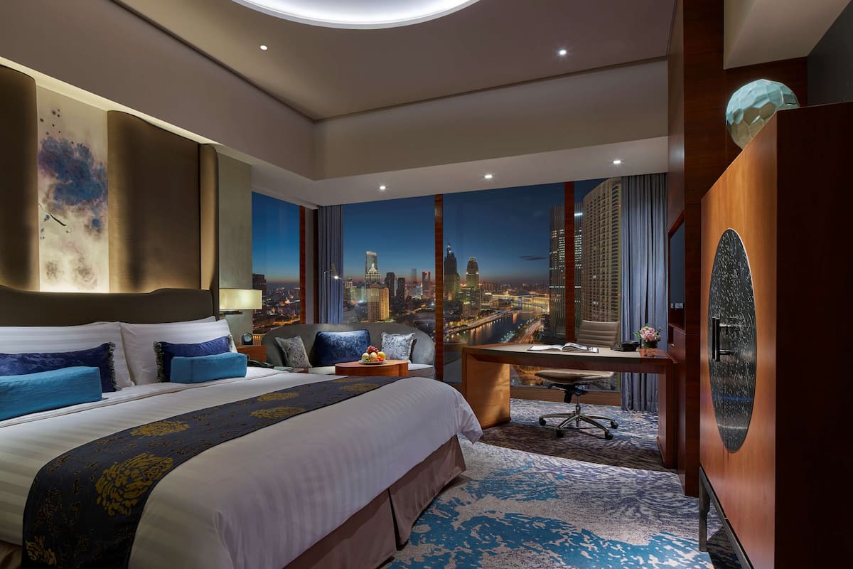 Quarto de hotel com uma cama grande, uma mesa e vista para a paisagem urbana.