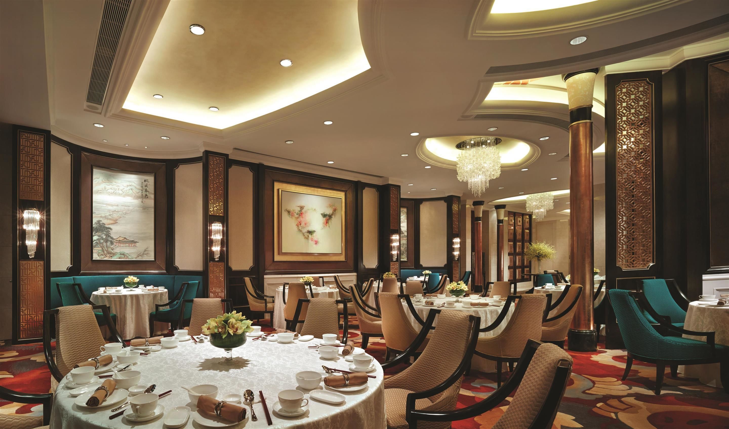 A hotel dining area with round tables, chairs, and chandeliers.