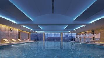 A large indoor swimming pool with a city view, modern ceiling design, and lounge areas.
