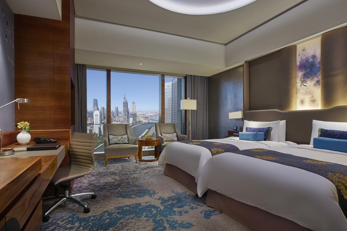 Une chambre d’hôtel avec vue sur la ville, deux lits, un bureau et une chaise.