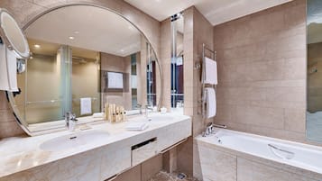 A modern bathroom with a large mirror, two sinks, a bathtub, and a glass shower enclosure.