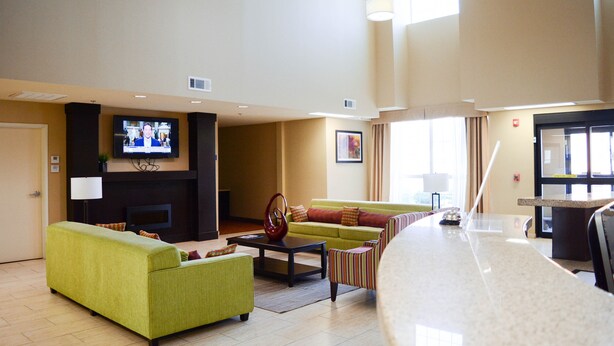 A spacious hotel lobby with a green sofa, a striped armchair, a coffee table, and a flat-screen TV mounted on the wall. - Cotulla Express Inn (Cotulla)