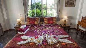 A hotel room with a large bed, two bedside tables with lamps, a view of greenery outside, and a framed picture on the wall. - Ya Nui Resort (Rawai)