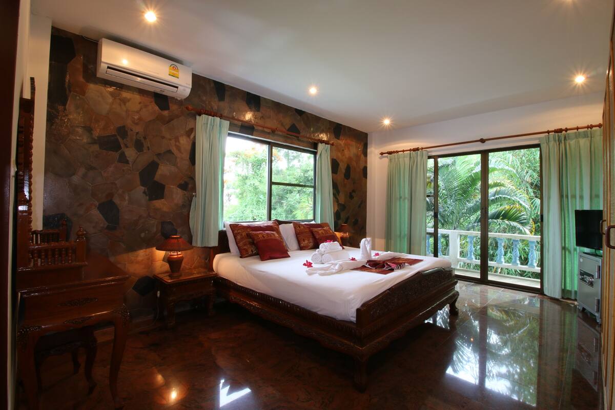 A spacious bedroom with a large bed, a wooden desk, a chair, and a television.