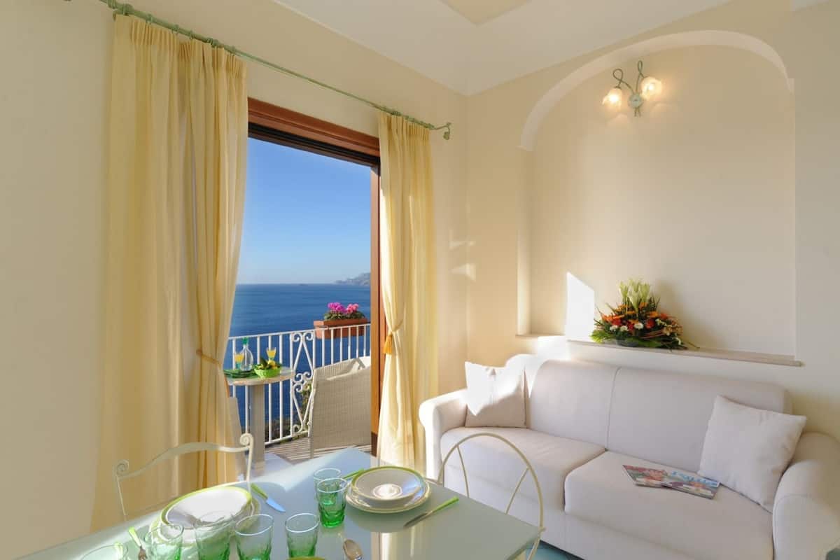 A balcony with a view of the sea, a white sofa, and a table set with glasses and plates.