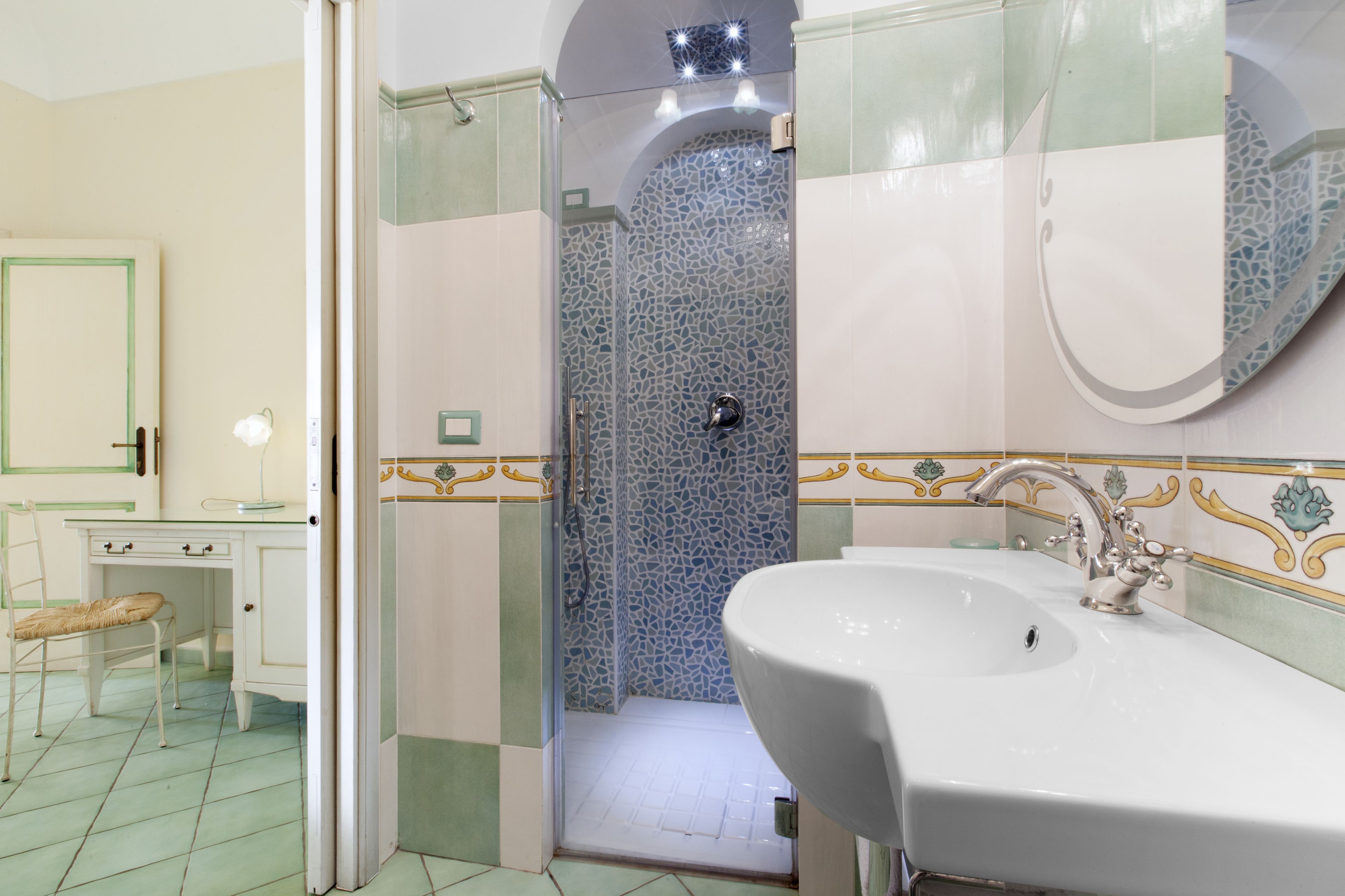 Een badkamer met een wit wastafelmeubel, een douche met glazen wanden en een spiegel met decoratieve tegels.