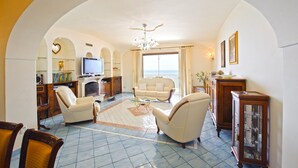 A spacious living room with a television, comfortable seating, and a view of the sea through large windows. - La Sorgente del Sole (Positano)