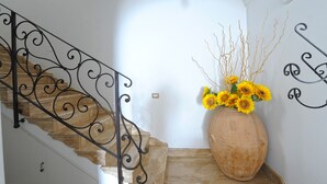 A staircase with a wrought iron railing, a large vase with sunflowers, and a wall-mounted light fixture. - La Sorgente del Sole (Positano)