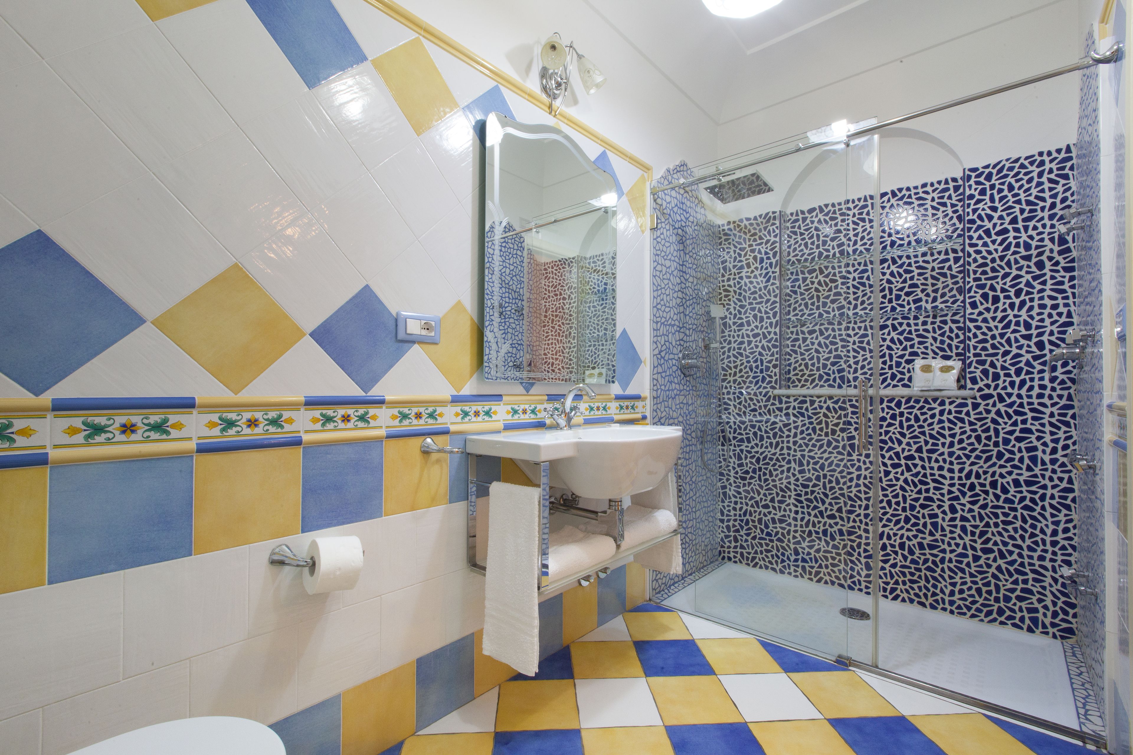 Une salle de bain avec un sol carrelé, un lavabo, un miroir et un espace douche.