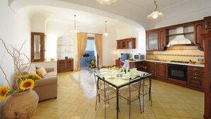 A spacious living area with a dining table, kitchen, and a view of the sea. - La Sorgente del Sole (Positano)