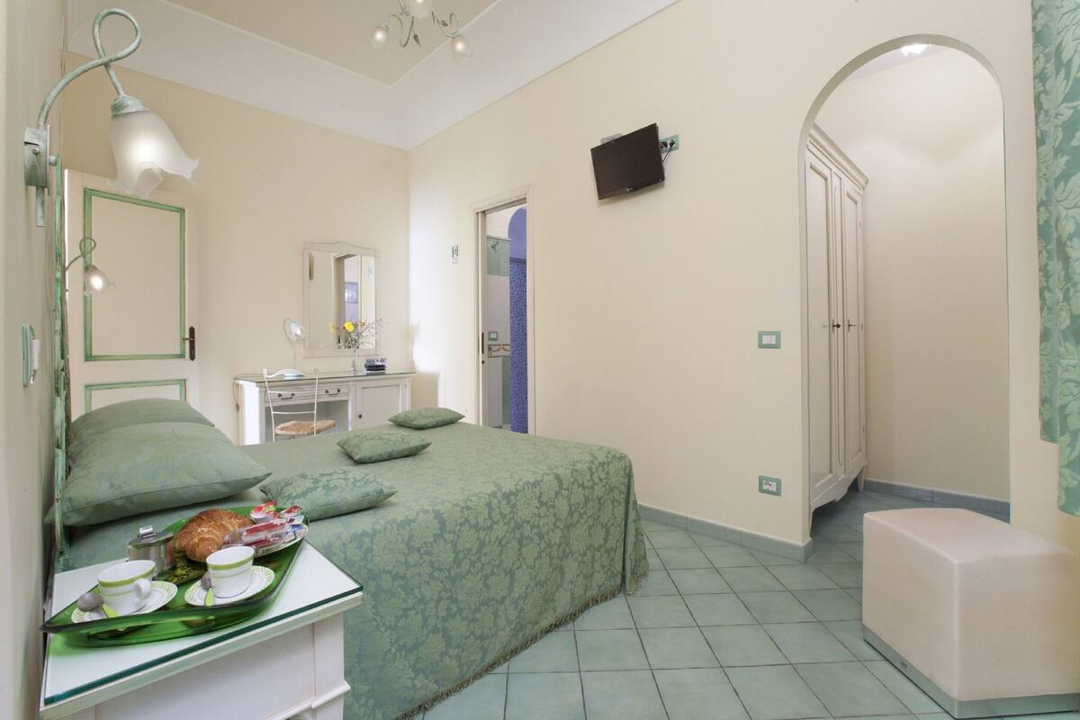 A bedroom with a bed, bedside table, lamp, and a small stool.
