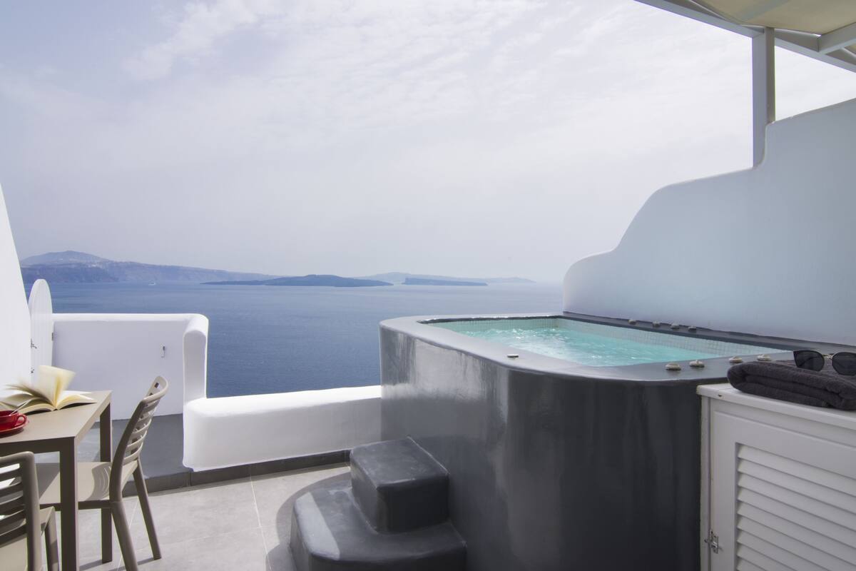 A balcony with a hot tub, a table with chairs, and a view of the sea.