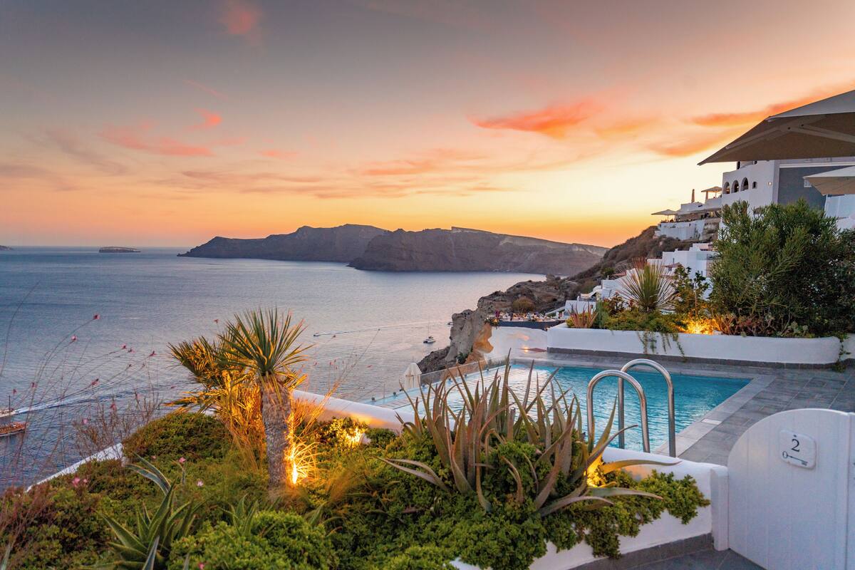 A pool area with a view of the sea and a mountainous landscape during sunset.
