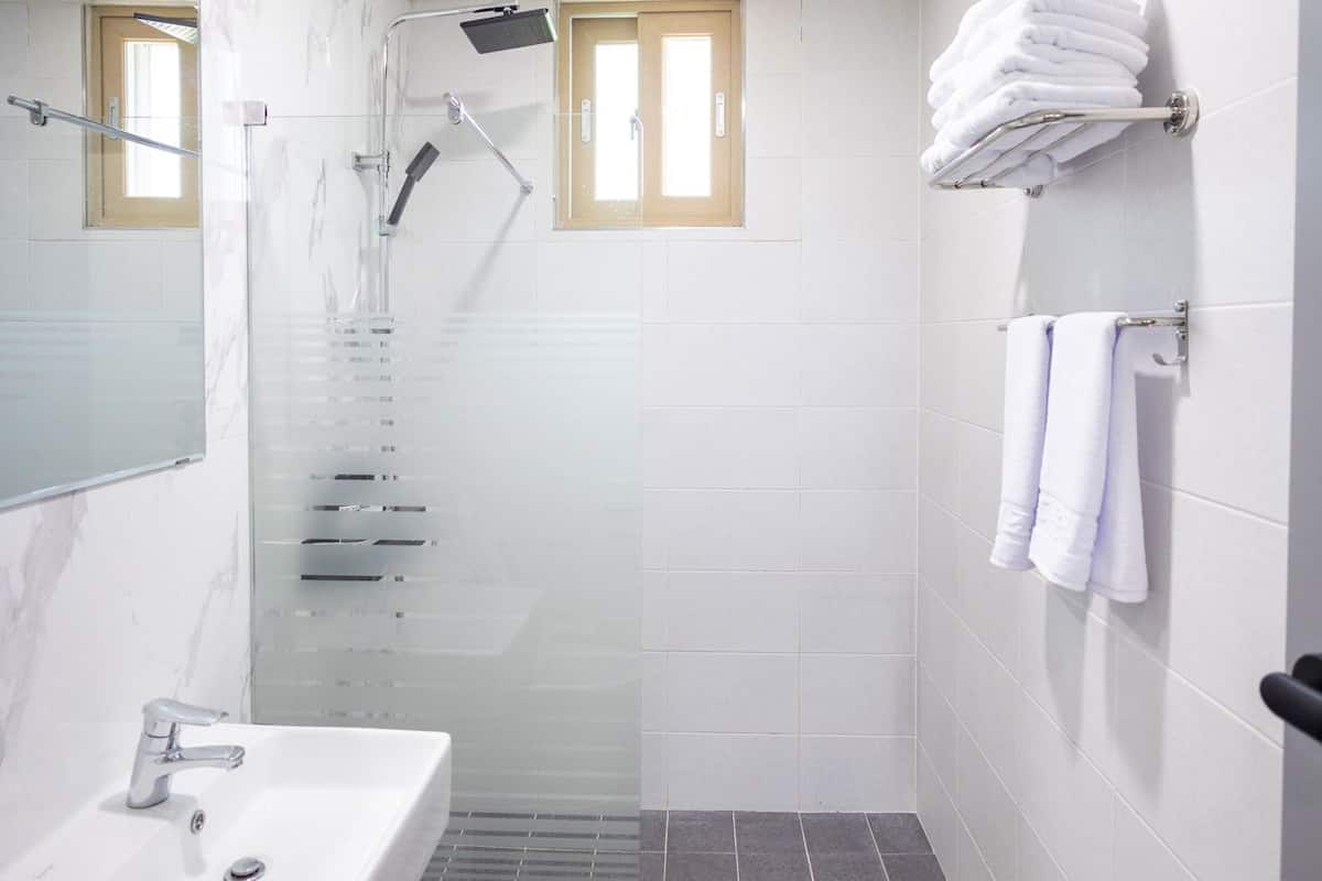 A bathroom with a sink, mirror, shower, and towel rack.