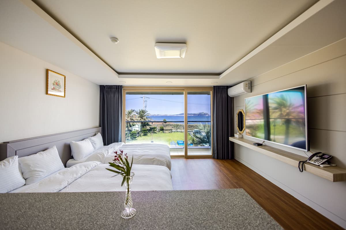 A hotel room with a large bed, a flat-screen TV, a phone, and a view of the ocean.