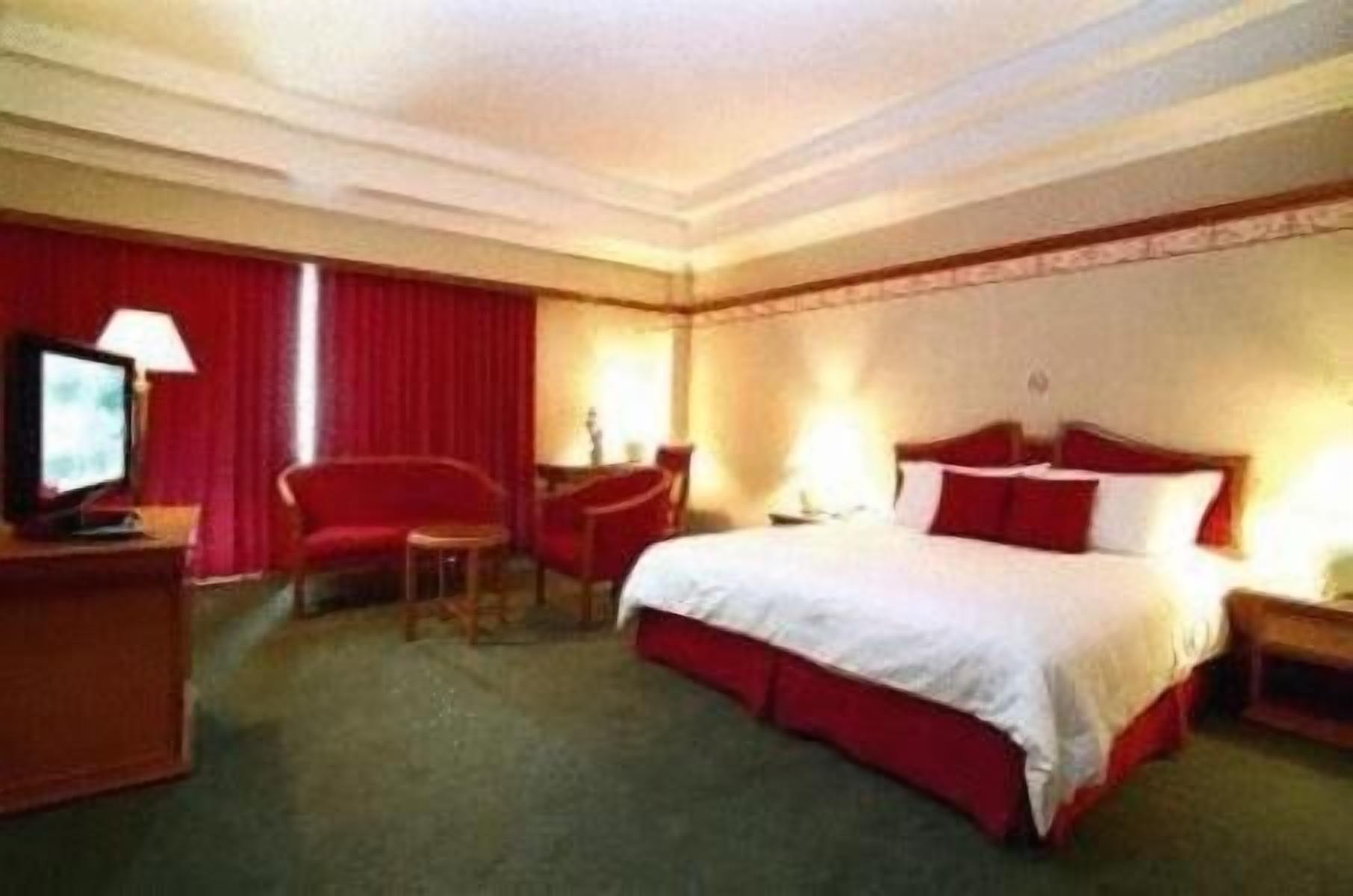 A hotel room with a bed, a desk, a chair, a TV, and a lamp.