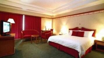 A hotel room with a bed, a desk, a chair, a TV, and a lamp.