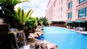 Una piscina con cascada, rodeada de vegetación y un edificio con varias ventanas.