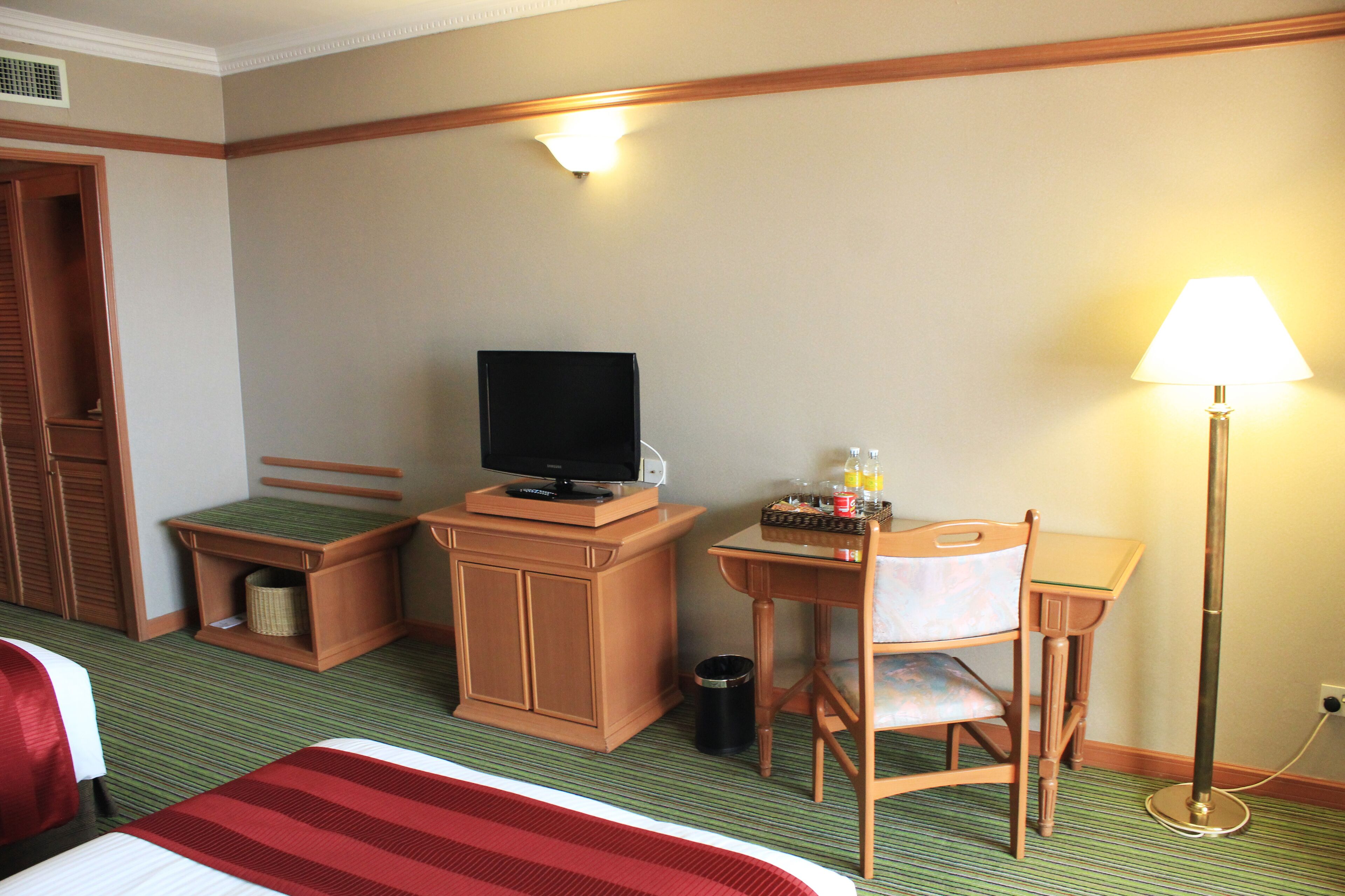 A hotel room with a bed, a desk with a chair, a television, a lamp, and a trash can.