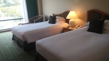 A hotel room with two beds, a nightstand with a lamp, a telephone, and a chair.
