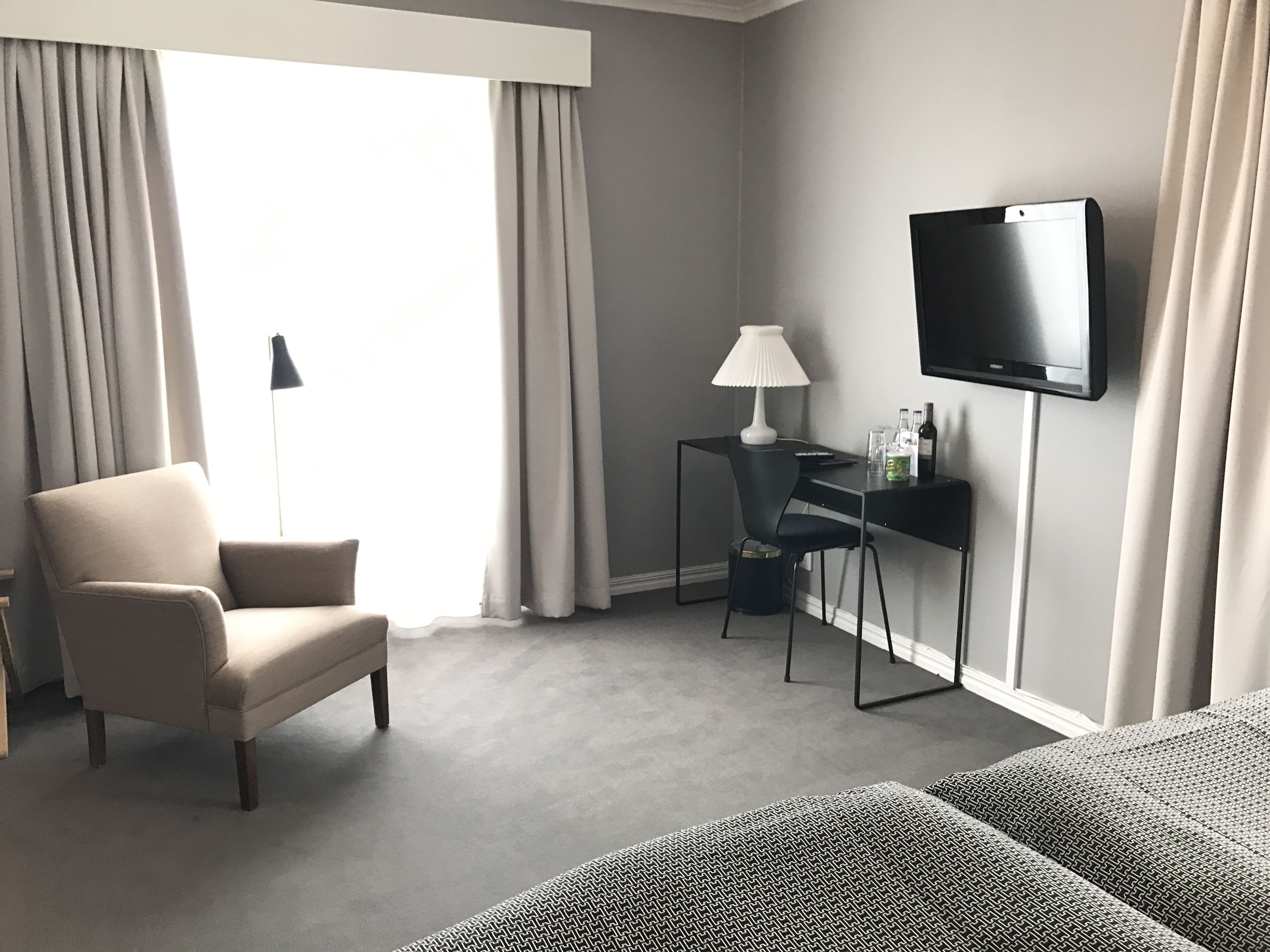 Una habitación de hotel con una cama, un escritorio con televisor, una silla y una lámpara.