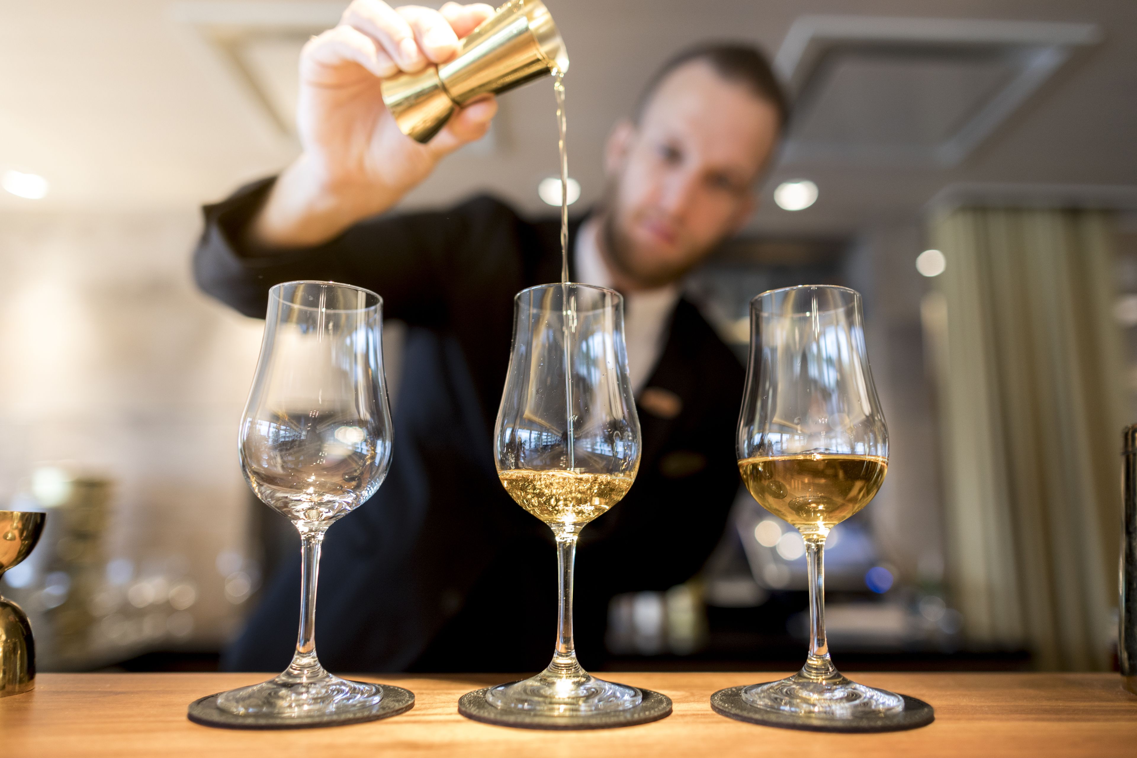 A person pouring a clear liquid into three glasses on a wooden table.