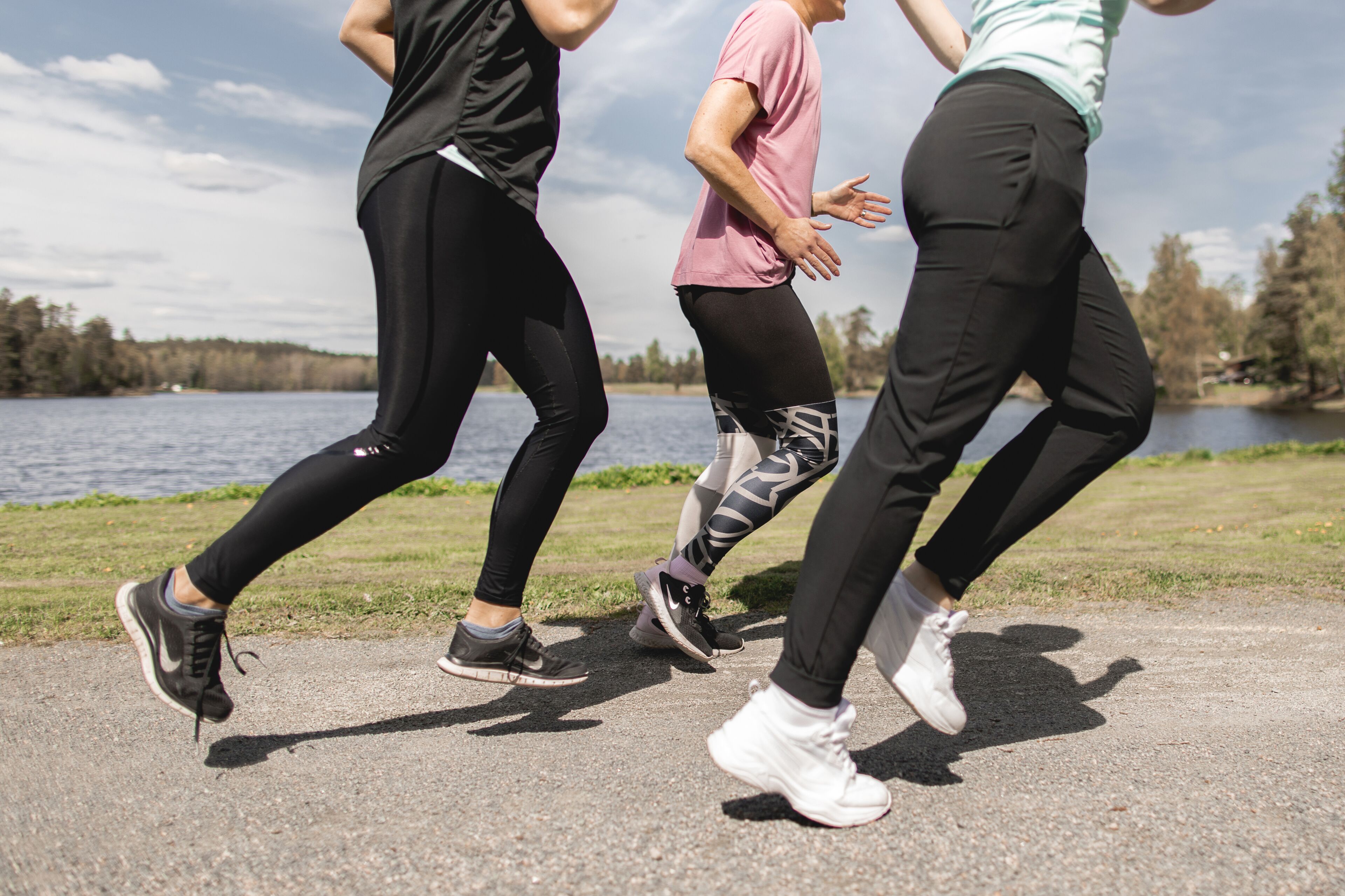 Three people jogging on a paved path near a body of water with trees in the background.