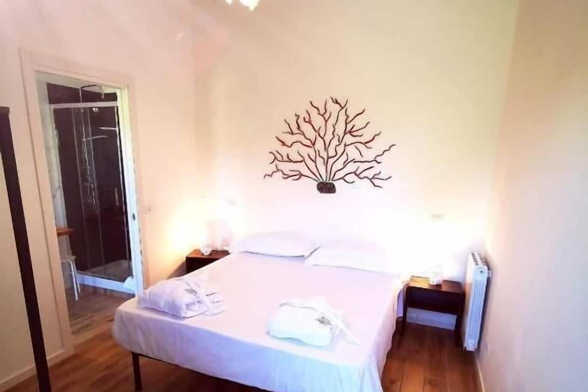 A bedroom with a bed, bedside tables, a radiator, a wall decoration, and a suitcase.