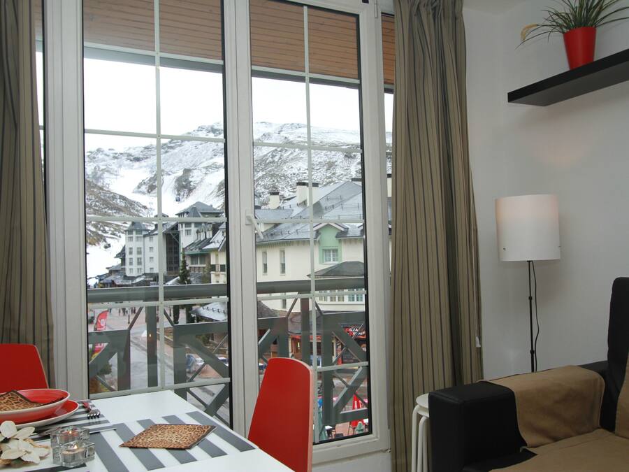 A room with a dining table, chairs, a lamp, and a view of a snowy mountain landscape through large windows.