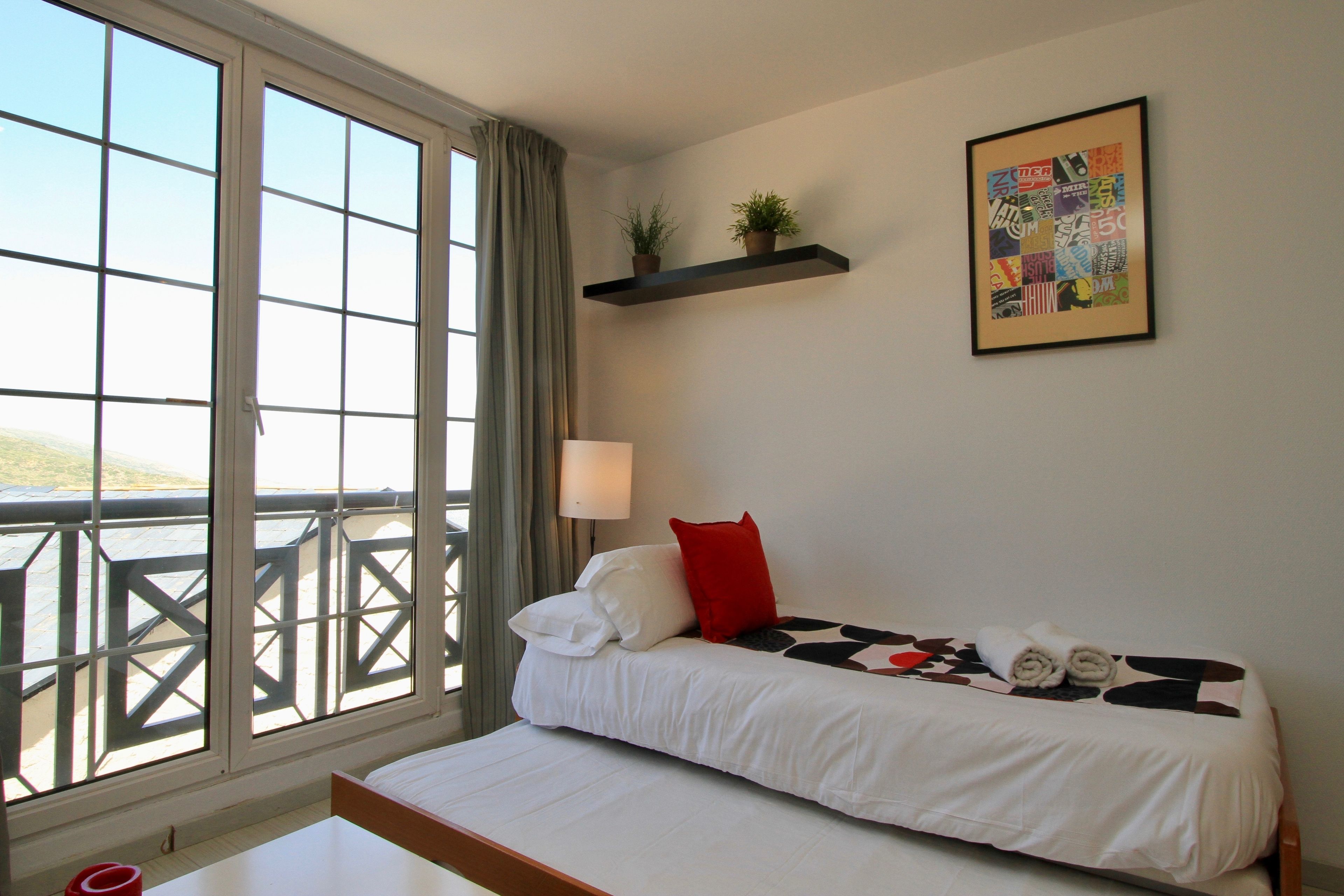 Une chambre d’hôtel avec un lit, une fenêtre donnant sur un beau paysage, une étagère fixée au mur avec des plantes et un tableau encadré.