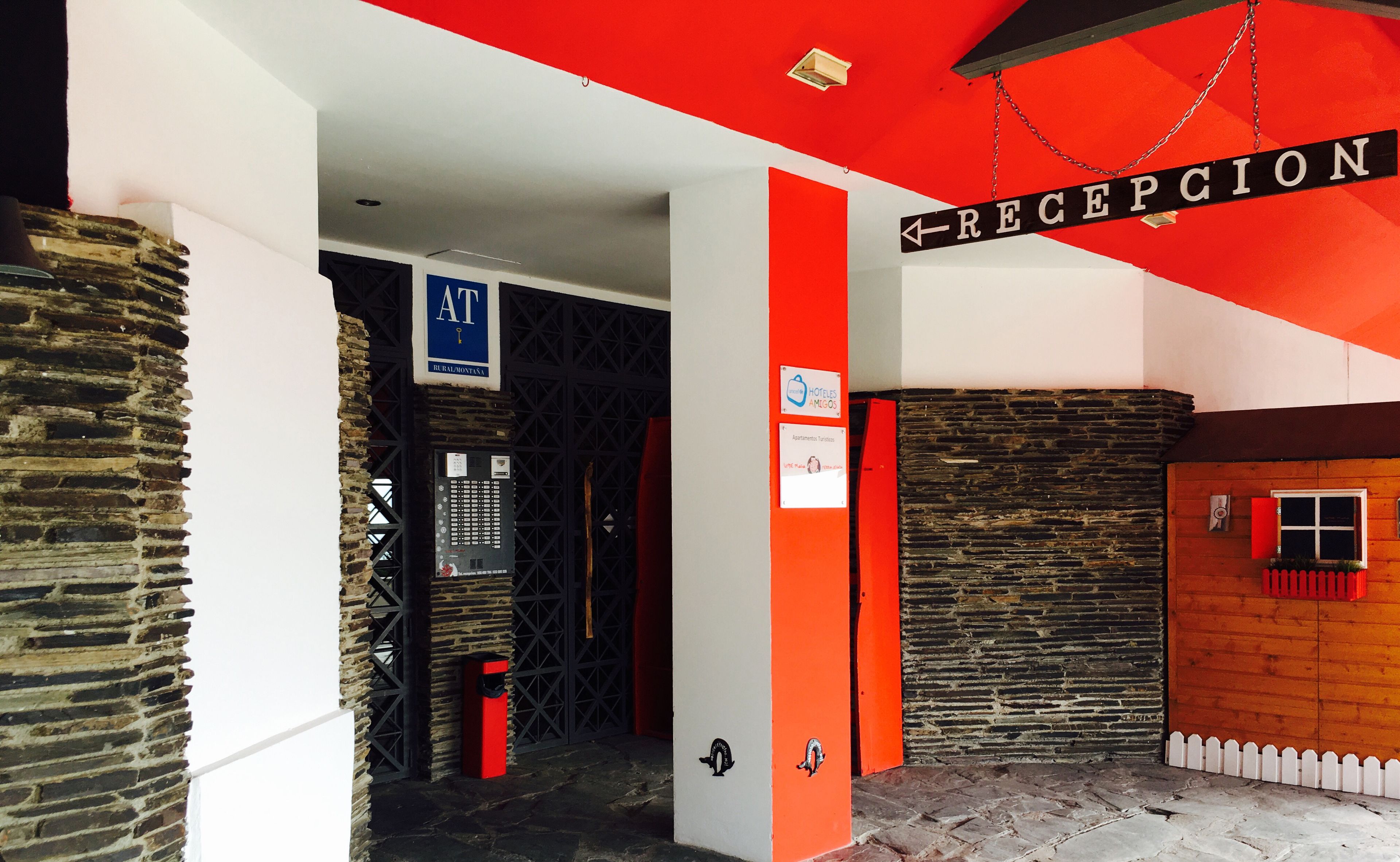 A reception area with a red and white color scheme, a reception sign, and a sign for "Apartamentos Turísticos".