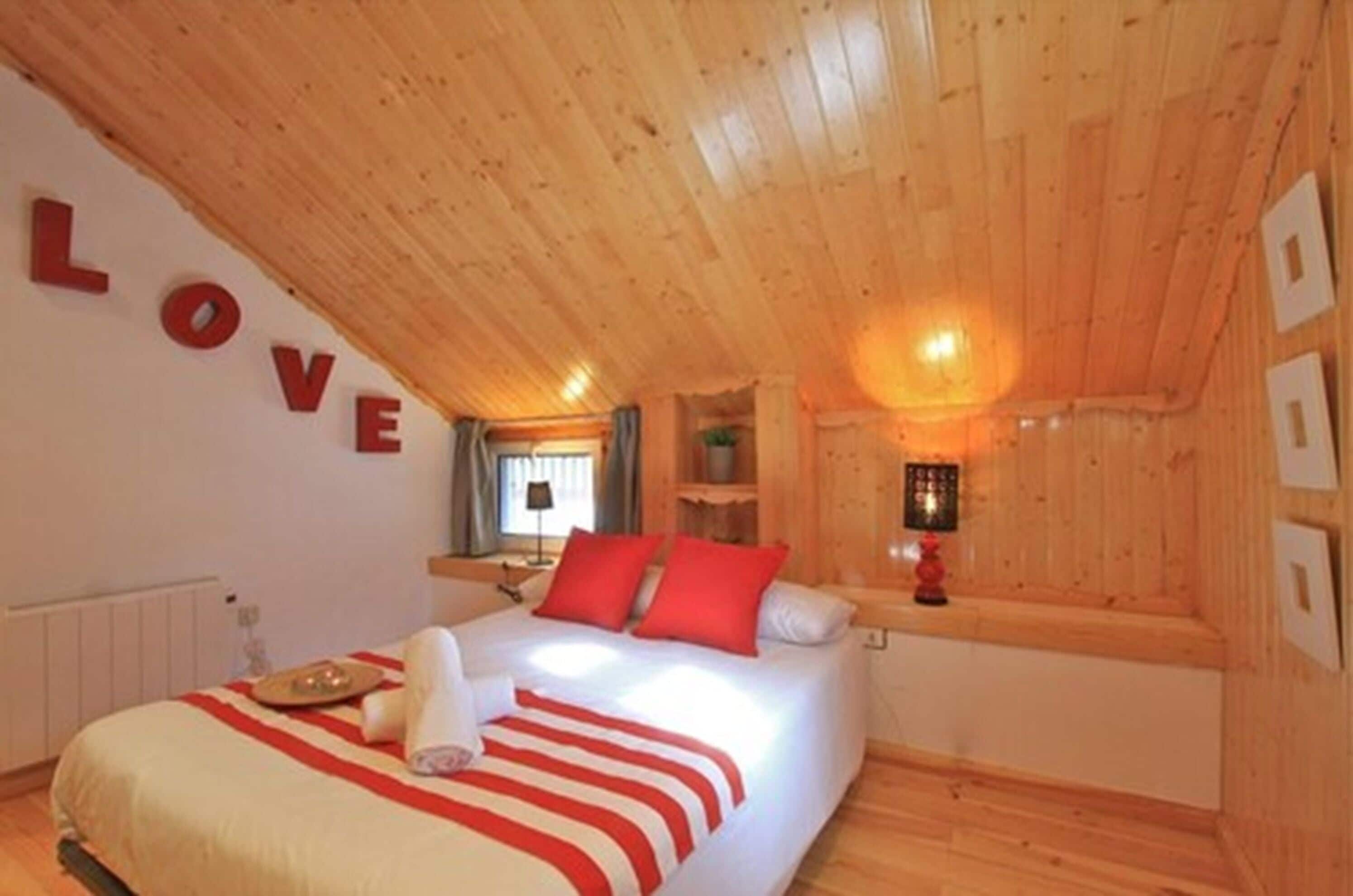 Une chambre confortable avec un plafond en bois, un lit recouvert d’une literie rouge et blanche, et un mur sur lequel le mot « AMOUR » est écrit en lettres.