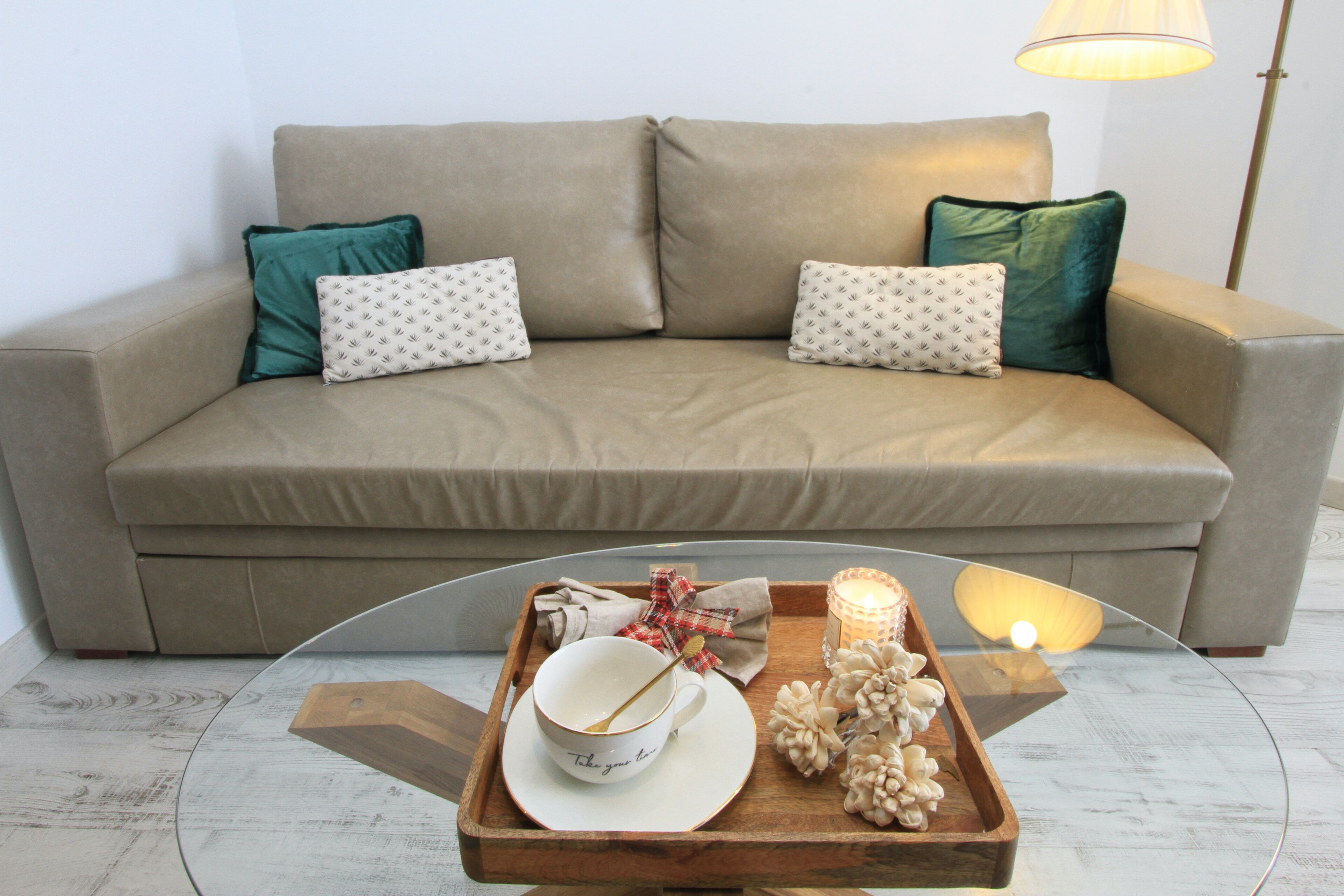 A beige sofa with teal pillows, a wooden tray with a bowl, a candle, and a lamp.