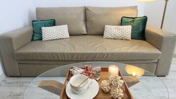 A beige sofa with teal pillows, a wooden tray with a bowl, a candle, and a lamp.