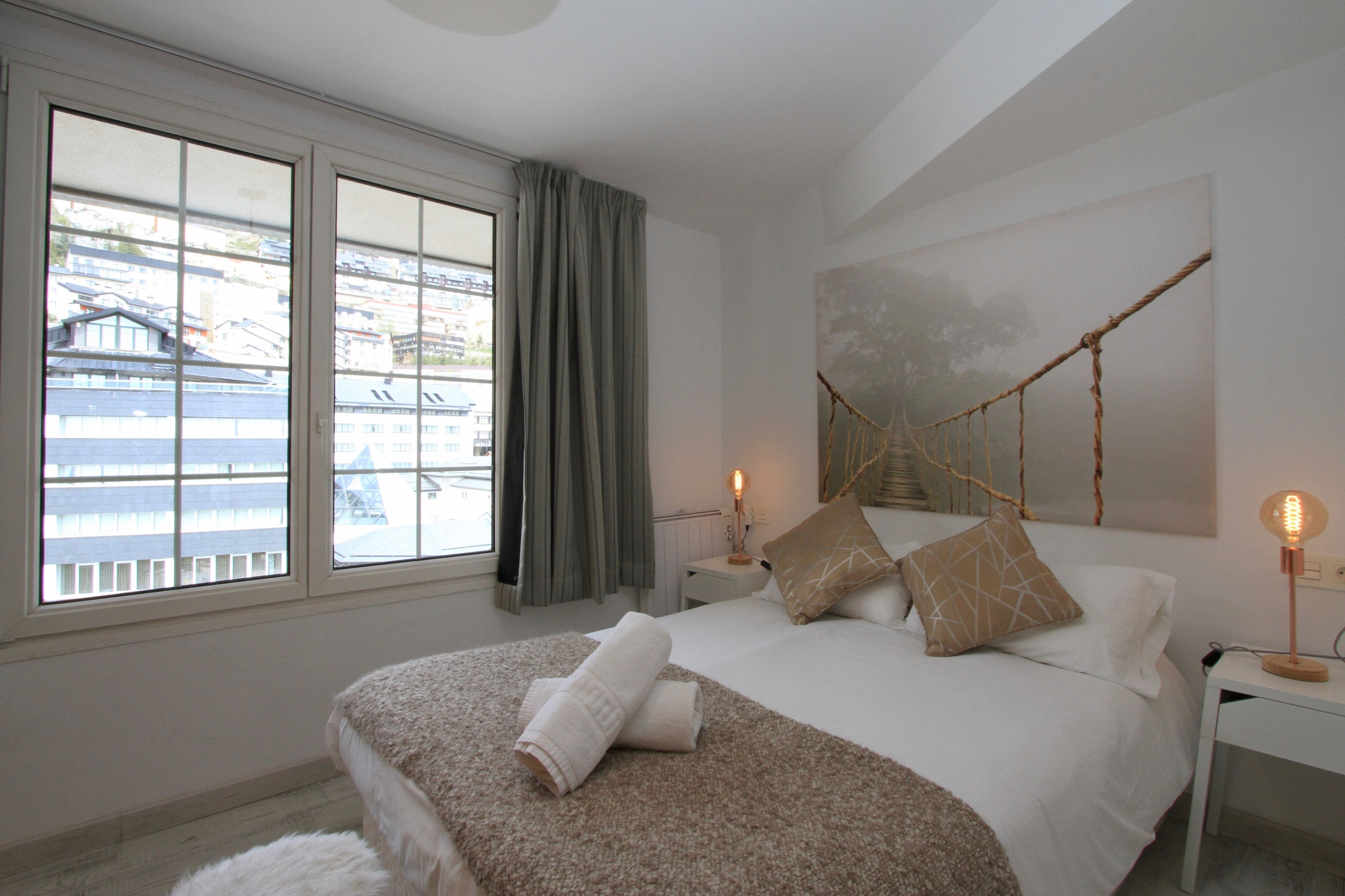 Une chambre d’hôtel avec un grand lit, une table de chevet, une lampe et une vue sur les immeubles par la fenêtre.