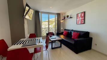 Una sala de estar moderna con un sofá de cuero negro, cojines rojos, una mesa de comedor con sillas rojas y un ventanal con vistas a la montaña.