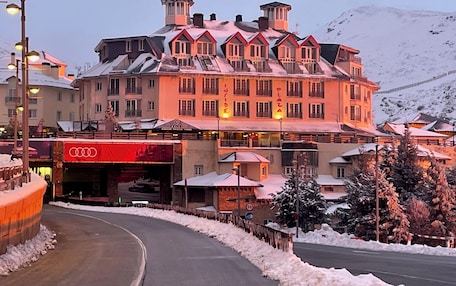 A hotel with multiple stories, a ski lift, and a mountain backdrop.