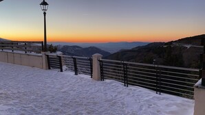 A snow-covered walkway with metal railings and a lamppost, leading to a scenic view of mountains and a sunset. - Inside Plaza Sierra Nevada (Monachil)