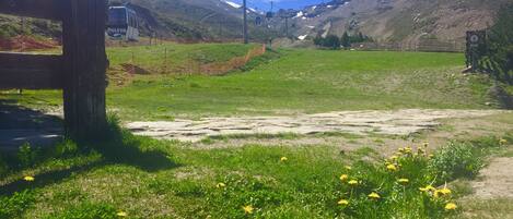 A mountainous landscape with a ski lift, a wooden fence, and a grassy area with yellow flowers.