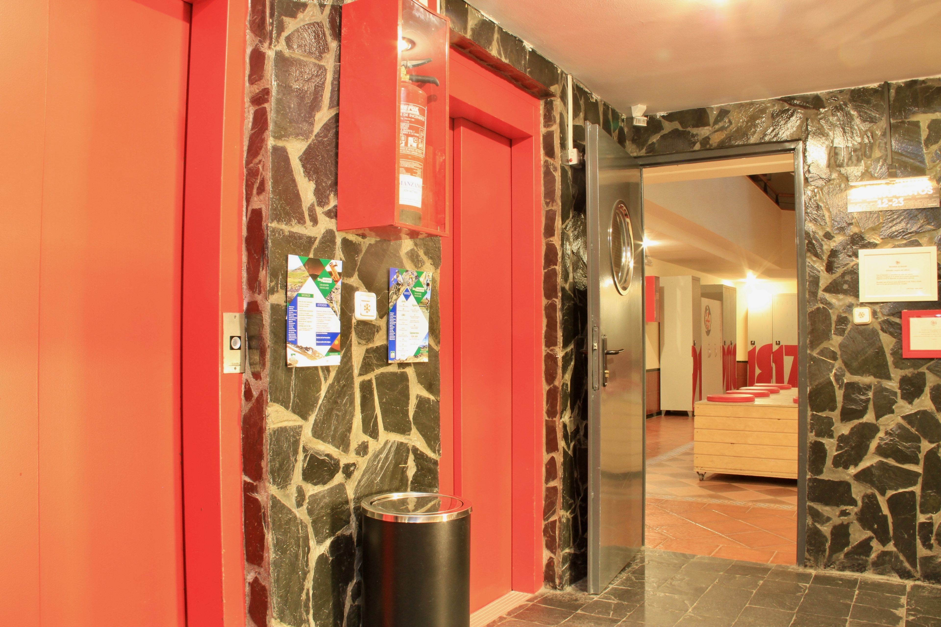 A hotel lobby with a stone wall, a red door, and a trash bin.