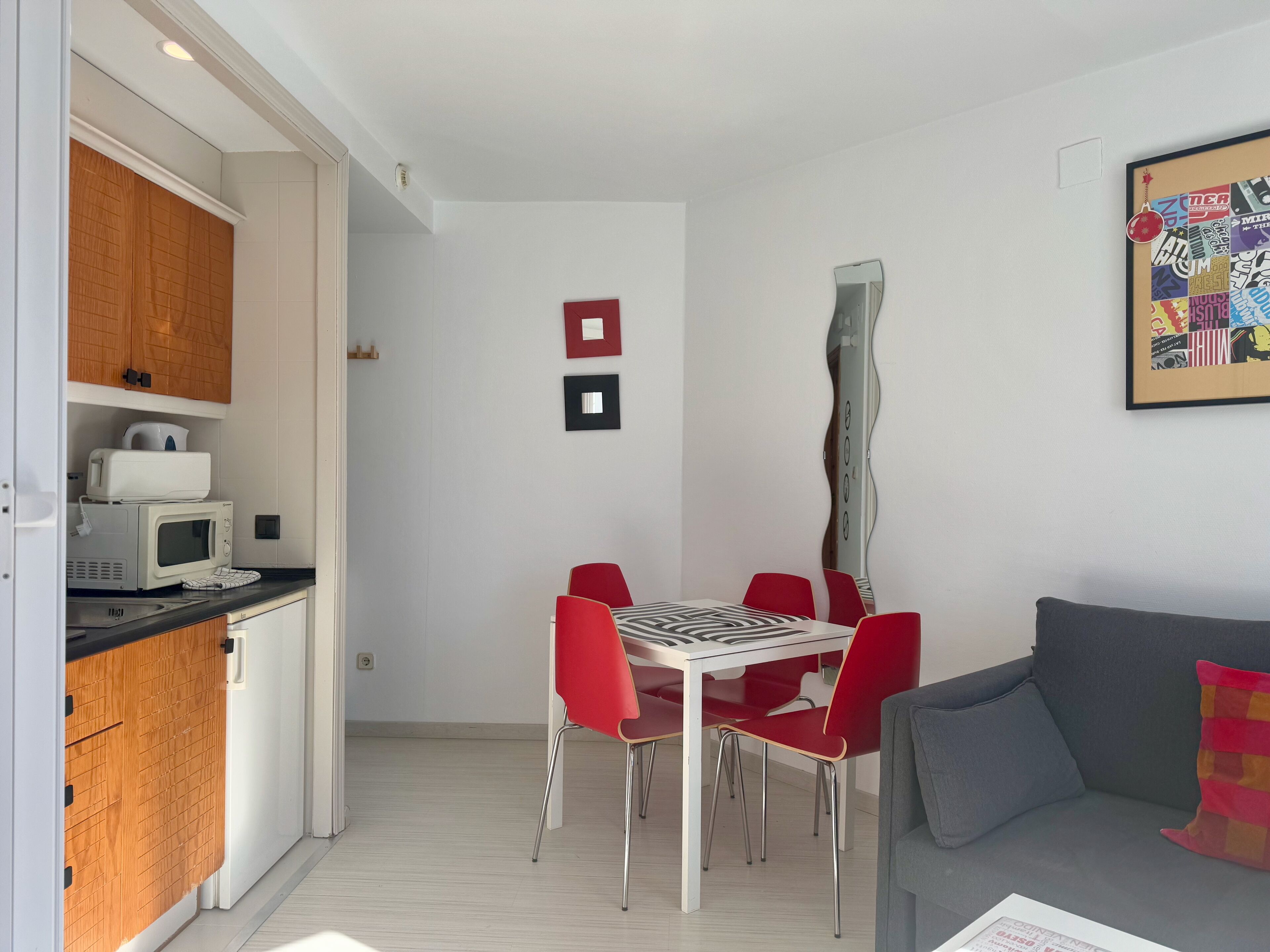 A compact living space with a kitchenette, a dining area with red chairs, and a grey sofa.