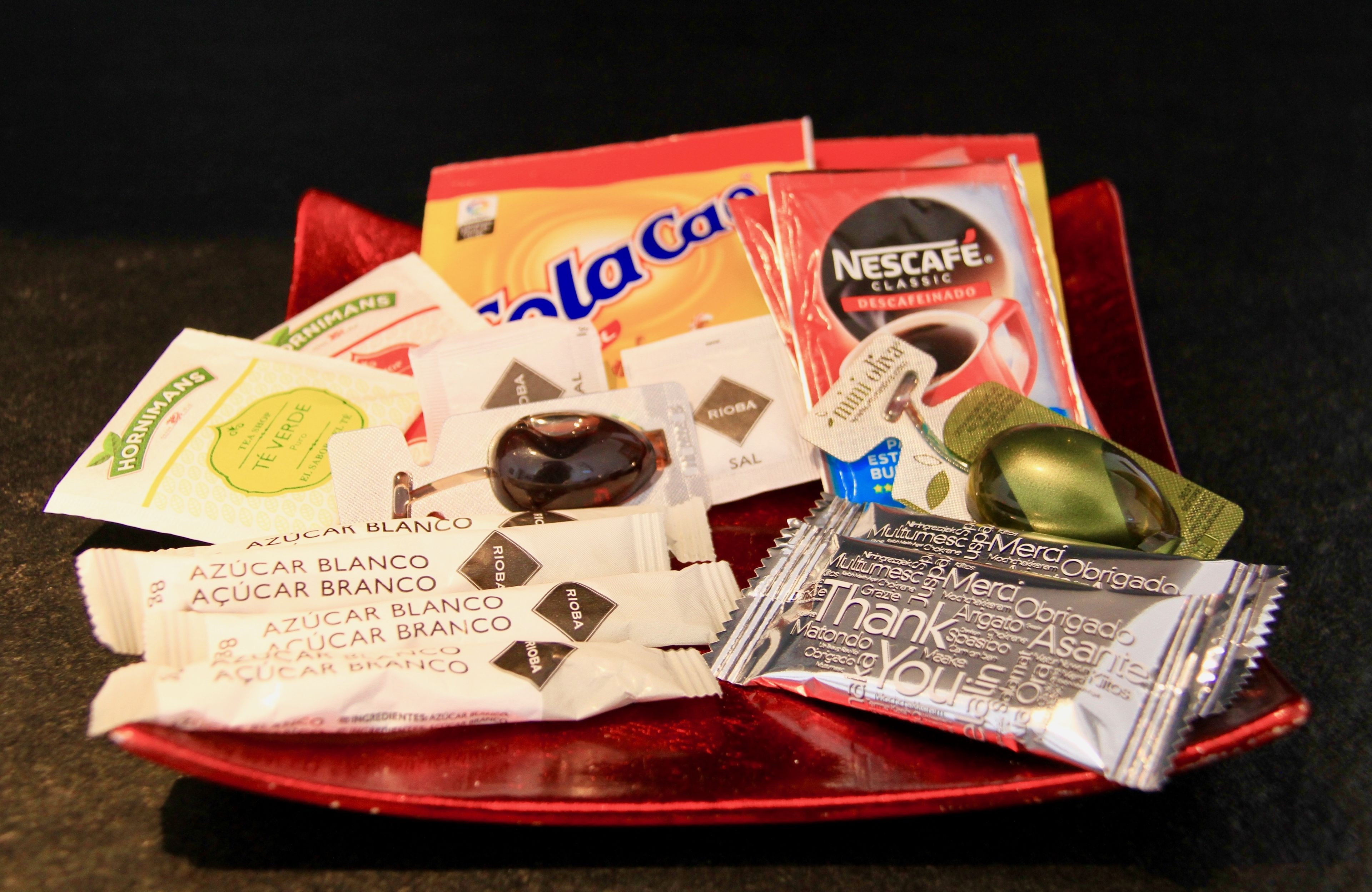 A tray with various food items including a red bag, a Nescafé Classic packet, and several chocolate bars.