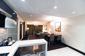 A modern hotel room with a kitchen area, a dining table with chairs, a sofa, and a chandelier. - Boudl AL Tahlia (Jeddah)